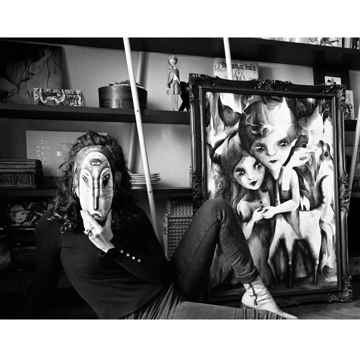Valentina Brostean en su estudio de Barcelona, sosteniendo una máscara pintada a mano junto a una de sus obras figurativas enmarcadas